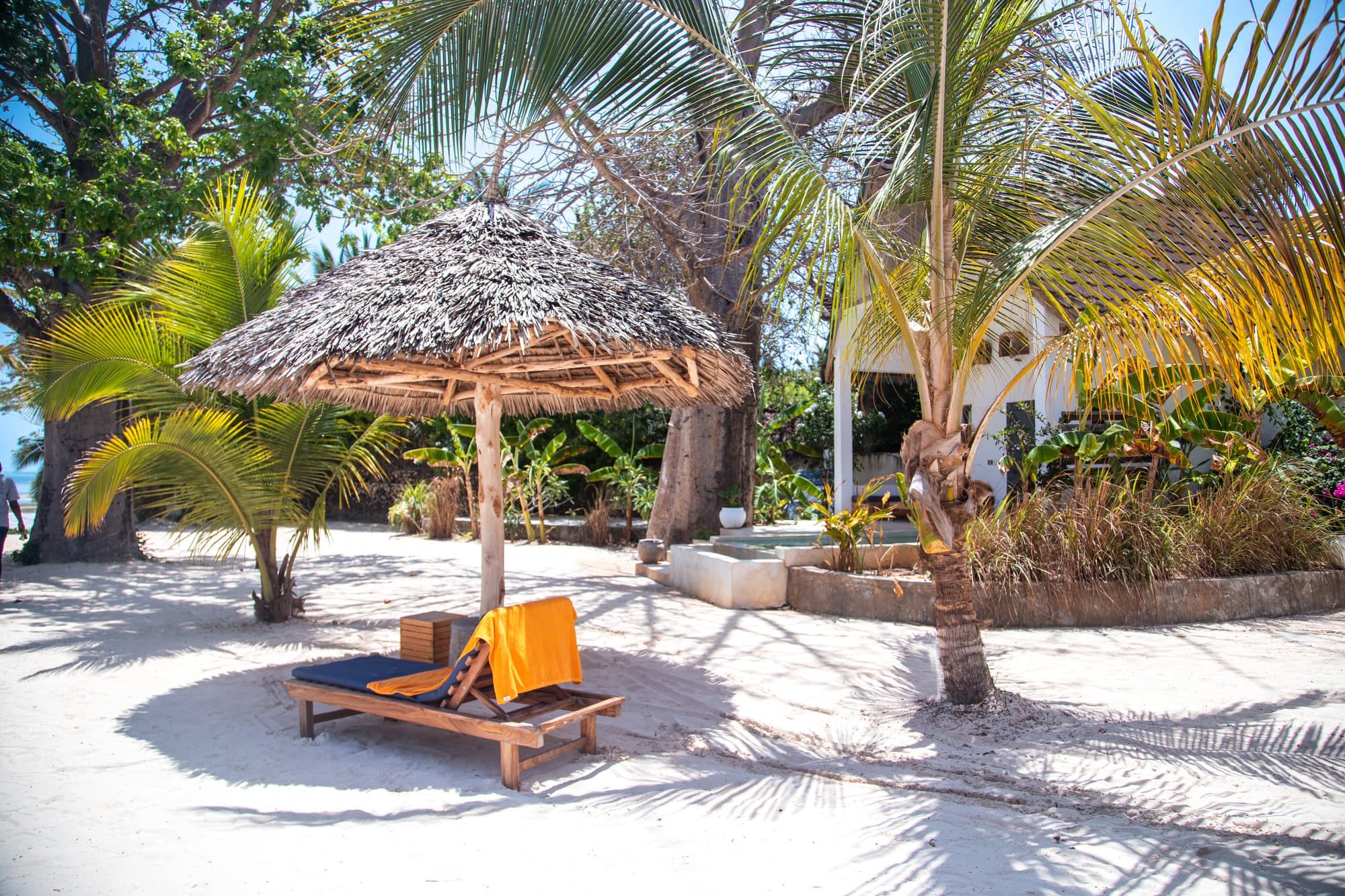 Strandliege unter einem Makuti-Sonnenschirm im Palmengarten eines Hotels auf Sansibar