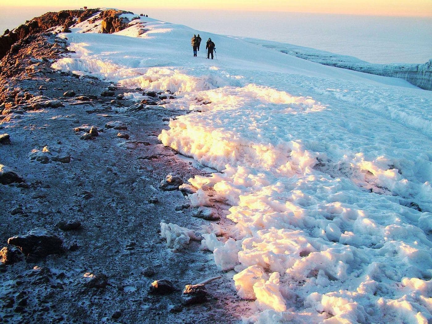 Bergsteiger auf dem schneebedeckten Kraterrand des Kilimandscharo bei Sonnenaufgang, über dem Wolkenmeer
