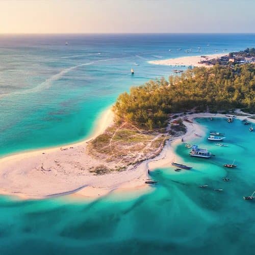 Luftaufnahme einer türkisfarbenen Bucht vor Sansibar mit Ausflugsbooten zu den Schnorchel-Spots
