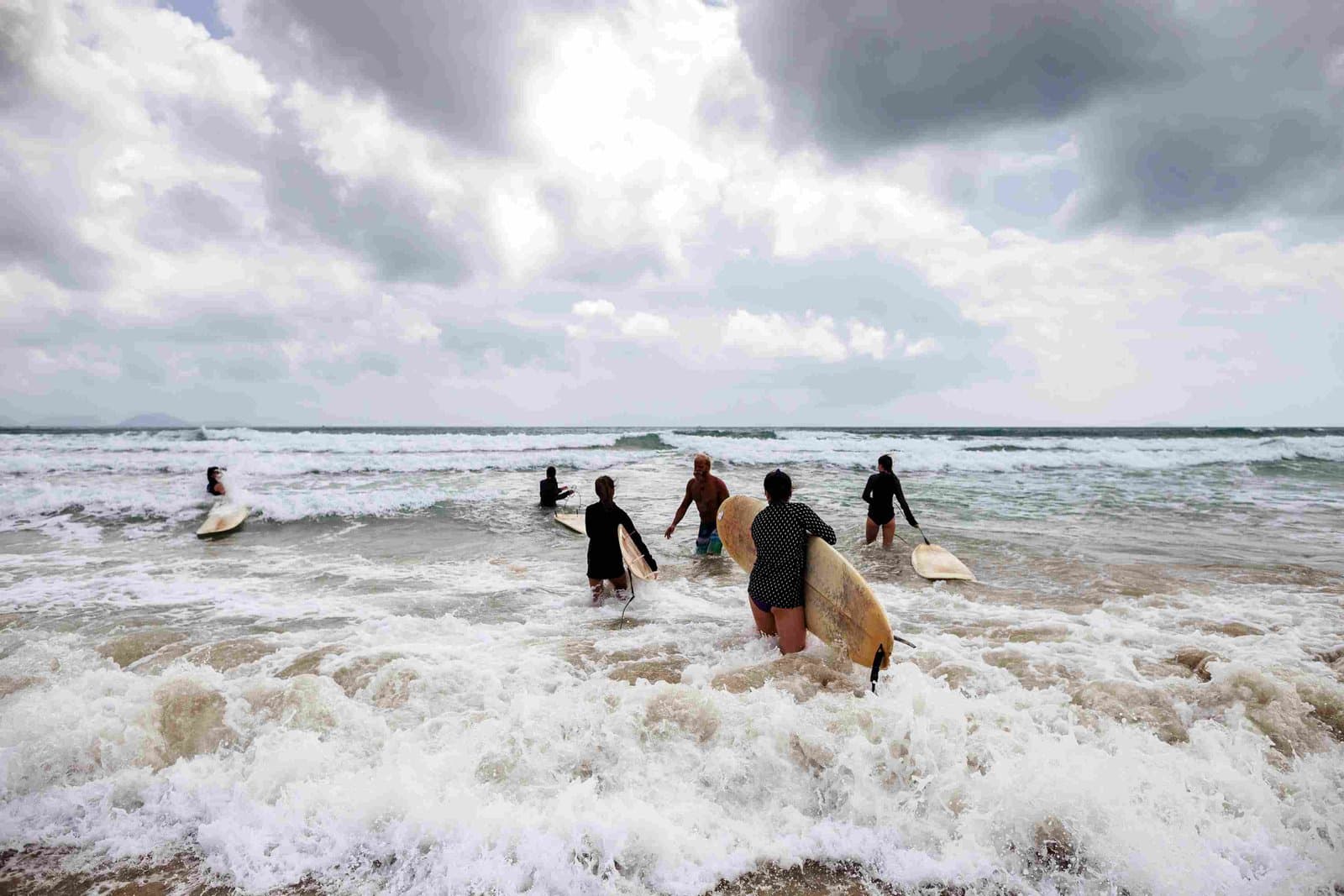 Surfer waten bei bewölktem Himmel mit ihren Boards ins Wasser vor Pangani